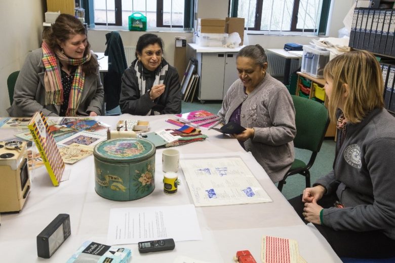 Two museum team ladies and two anand mangal ladies sat at a table looking at scraps of fabrics