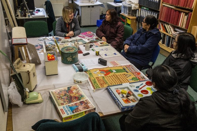 Museum worker talking to three anand mangal ladies at a table with books and posters on it