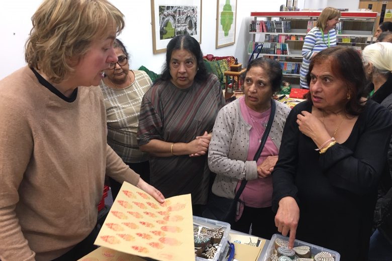 Art workshop leader holding a patterned print while talking to four ladies