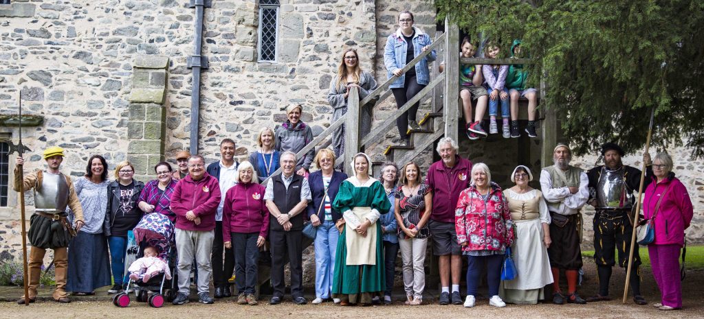 A big group photo of volunteers at the 1620s house and garden. some volunteers are in costume as maids or knights.