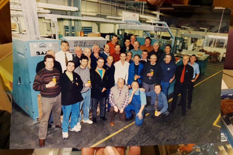 90s photo of a large group of men in a book printing factory