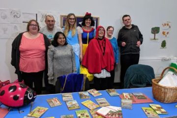 Participation workers dressed up as Cinderella, Snow White and Little Red Riding Hood stood with a group of people. They're in front of a table with several Ladybird books on top.