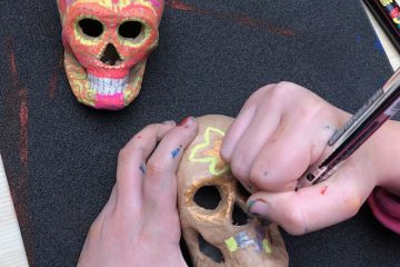 Hand drawing on clay skull. completed coloured clay skull in the background.