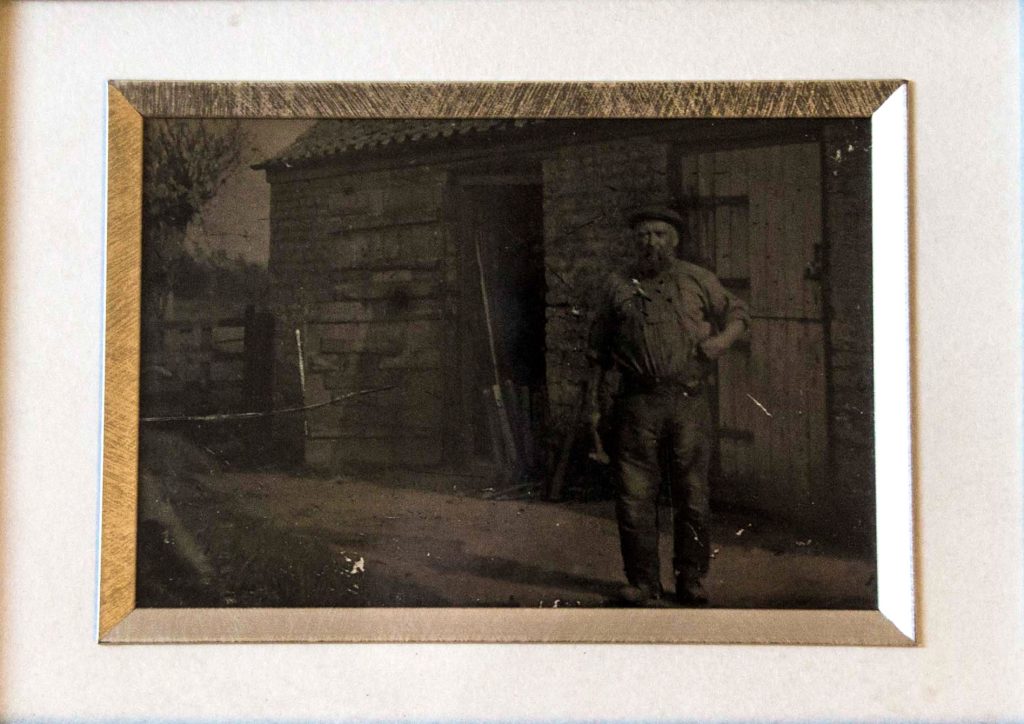 Old photograph of a man wearing work clothes stood outside a wooden shop