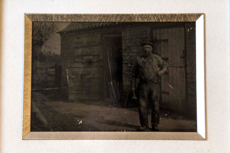 Old photograph of a man wearing work clothes stood outside a wooden shop