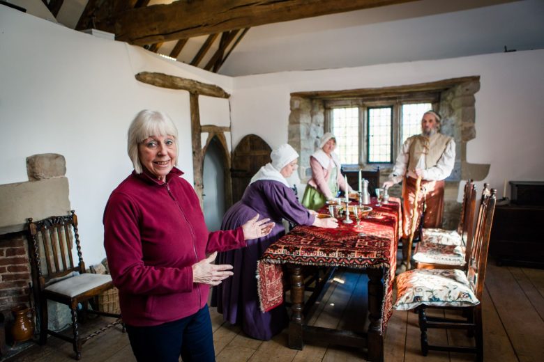 Volunteer pointing behind her to other volunteers in period costumes around a dining room.