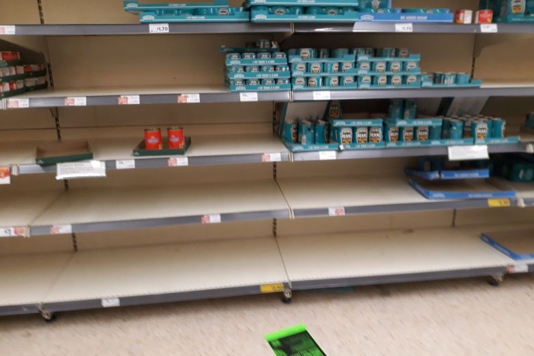Supermarket shelf that is scarce of many items. only some tins of beans.