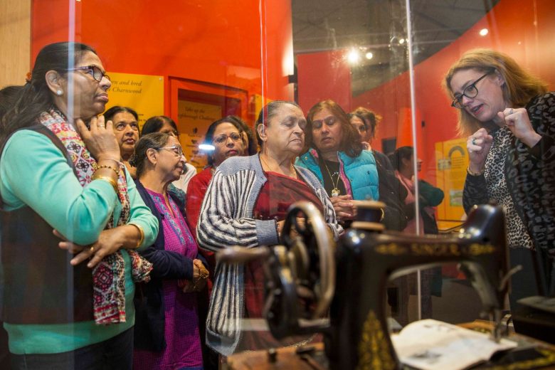 Senior curator showing the Anand Mangal ladies a museum display case of a vintage sewing machine