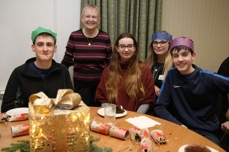Two adults and three teenagers wearing paper crows sat at a table with coffee and christmas crackers