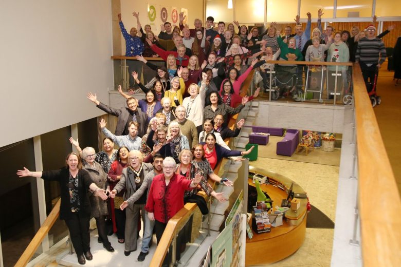 Big group photo taken on the stairs. They're raising their arms and smiling.