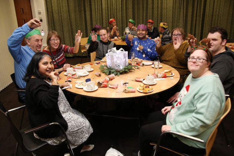 People wearing paper crowns sat around two tables with coffee and christmas crackers