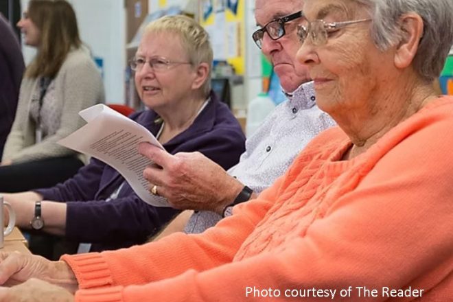 3 elderly people sat at a table. One man is reading a piece of paper.