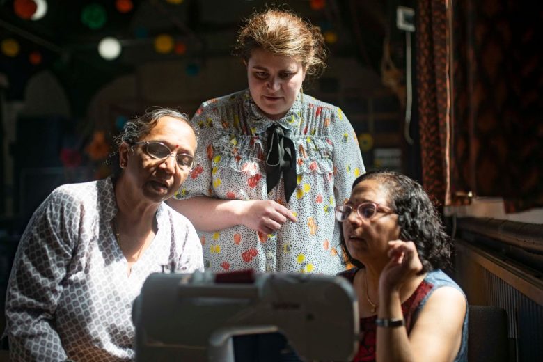 Workshop leaders stood behind two ladies sat at a sewing machine.