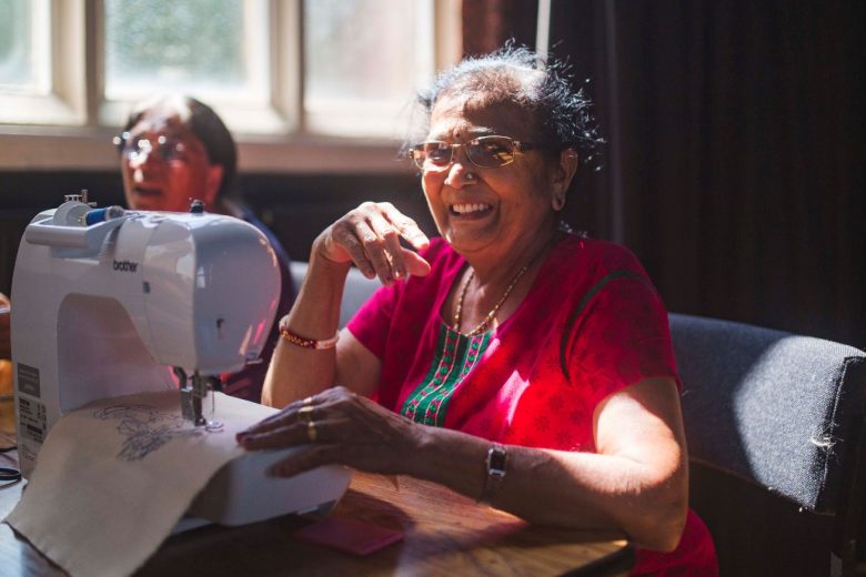 Anand Mangal lady smiling. She is using a sewing machine.