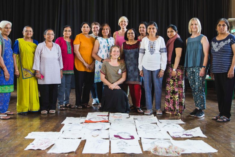 Anand Mangal ladies, participation workers and workshop leaders pose for a group photo. Stitched self portraits lie on the floor in front of them.