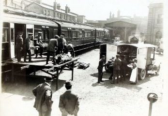 Black and white photo of a train. Men are carrying things off it and over to a vehicle.