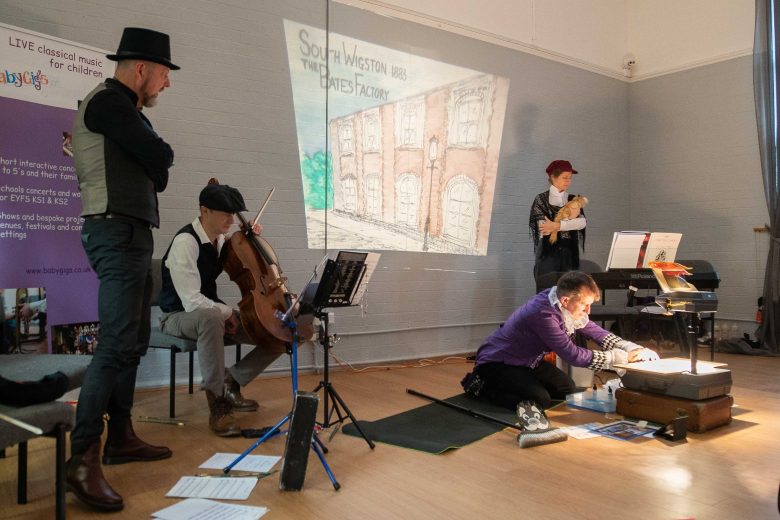 A group of musicians setting up and looking at sheet music. One is sat down with a cello.