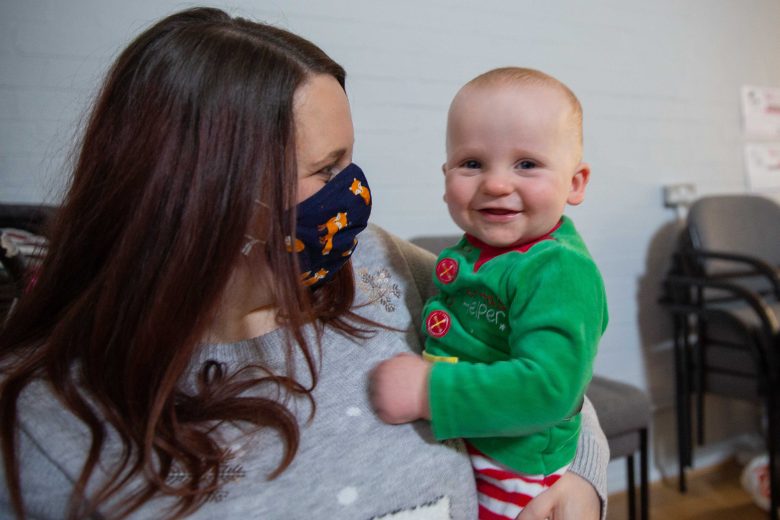 A woman wearing a mask holding a smiling baby