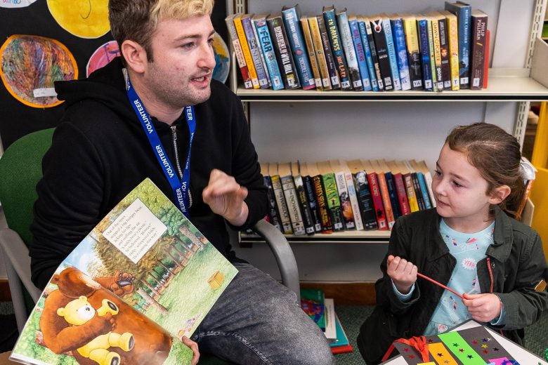 A volunteer reading a picture book to a child in a library