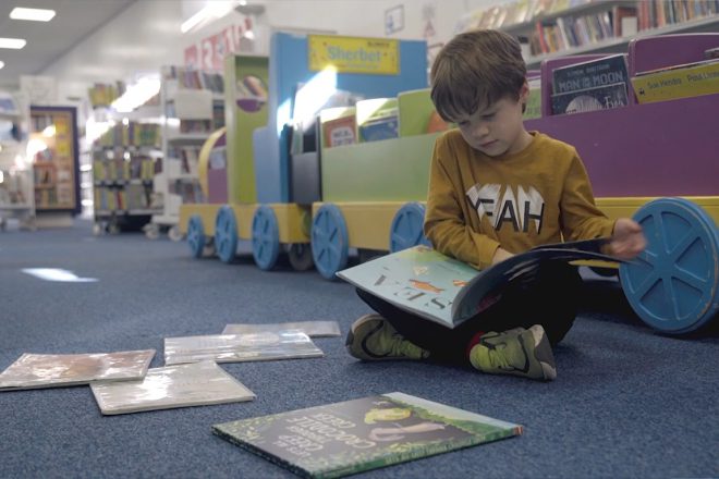 Young boy sat on a library floor reading a picture book