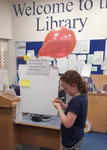 A young girl stood in the library and writing on a post-it note