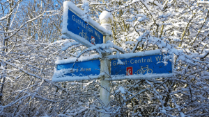 Great central way signpost topped with snow. snowy trees in the background.