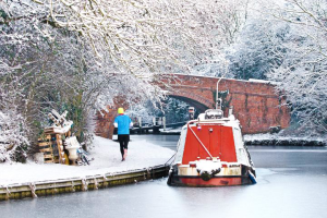 Canal towpath and trees covered in snow. Canal boat on the water.