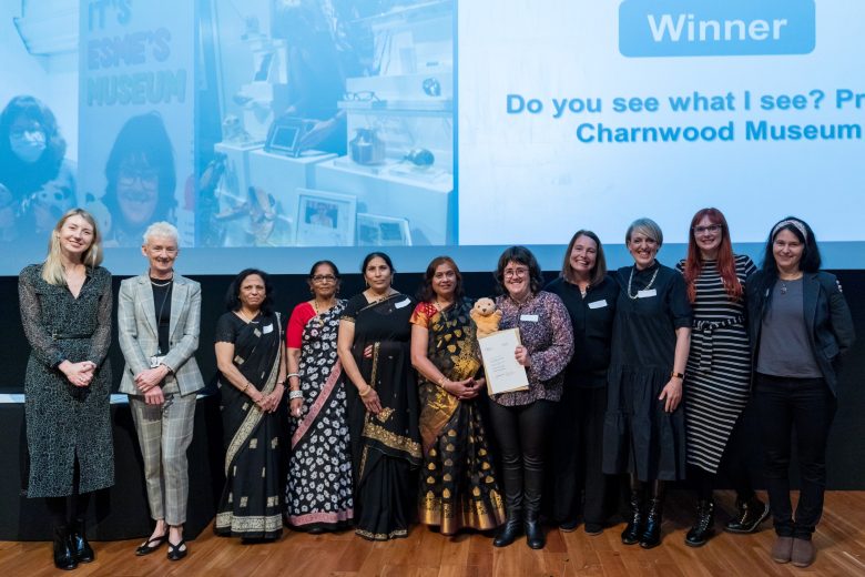 A group of volunteers and participation team members standing on a stage. one volunteer is holding a certificate.