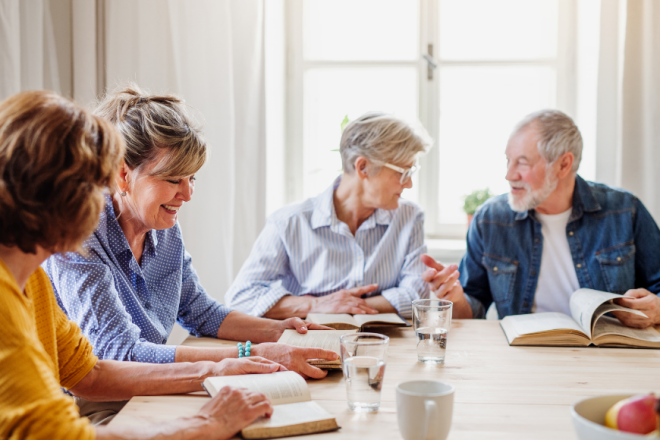 Four adults sat talking at a table. They each have a book in front of them.