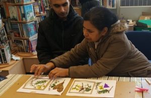 A woman and a man sat at a table looking at dried flower pressings.