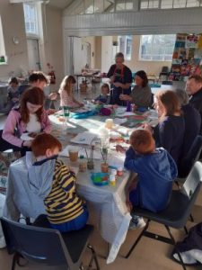 Adults and children sitting at craft tables. they are working on their patches.