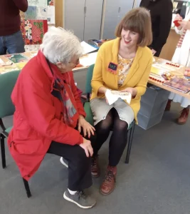 A woman stitching her patch, chatting to an elderly lady