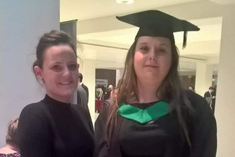 Two women stood together for a photo. One is wearing a graduation cap and gown.
